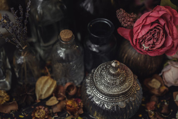 vintage jars, bottles, containers, flowers in smoke and dry leaves on a wooden table with warm light