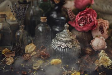 vintage jars, bottles, containers, flowers in smoke and dry leaves on a wooden table with warm light