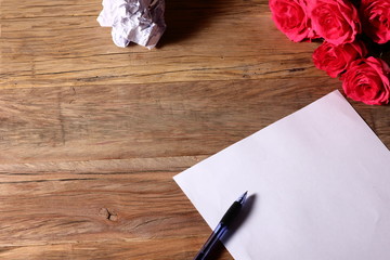 background with red flowers and a pen on a blank sheet of paper