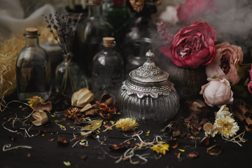 vintage jars, bottles, containers, flowers in smoke and dry leaves on a wooden table with warm light