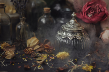 vintage jars, bottles, containers, flowers in smoke and dry leaves on a wooden table with warm light