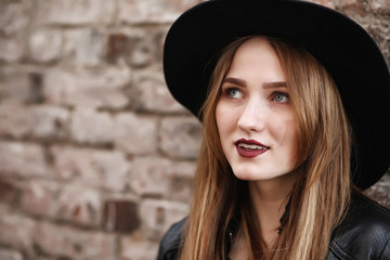 Young beautiful girl in a hat and with a dark make-up outside. Girl in the Gothic style on the street. A girl walks down the city street in a leather waistcoat with a phone.