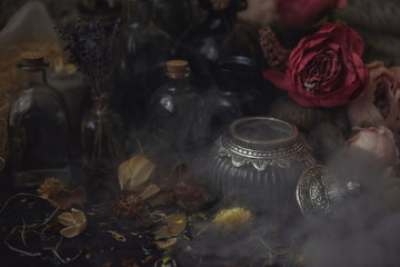 vintage jars, bottles, containers, flowers in smoke and dry leaves on a wooden table with warm light