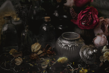 vintage jars, bottles, containers, flowers in smoke and dry leaves on a wooden table with warm light