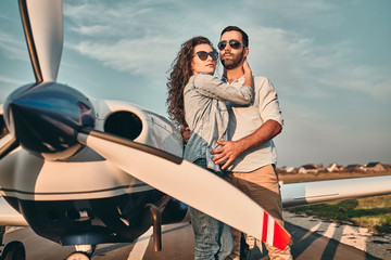 Beautiful and happy young couple posing in front of an old retro private propeler airplane