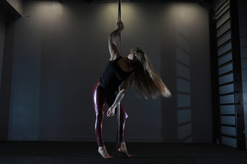 The dancer on the pylon in the studio. Girl doing exercises on a sports equipment.