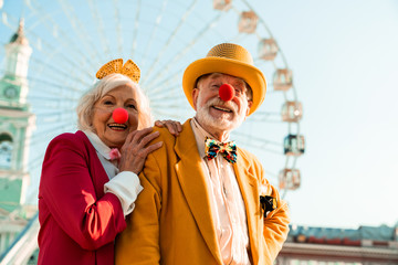 Funny senior couple in clown noses standing near ferris wheel
