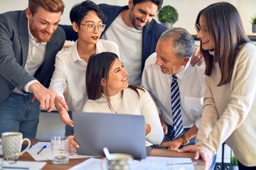 Fototapeta premium Group of business workers smiling happy and confident. One of them sitting and partners standing around. Working together with smile on face looking at the laptop at the office