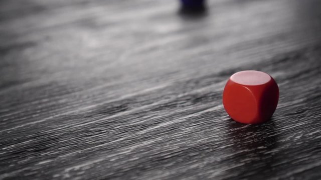 Three multi-colored game dice fall on a black textured old wooden table. Bounce and spin. Red, yellow and blue. The concept of gambling and good luck. Slow motion.