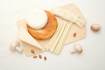 Fototapeta na wymiar Various types of cheese, smoked, pigtail, hard varieties, are located on a wooden Board, decorated with mushrooms, on a white background. The concept of cheese.