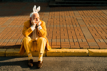Senior man in in funny accessories resting in the city