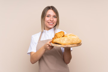 Young blonde girl with apron. Female baker holding a table with several breads with happy expression