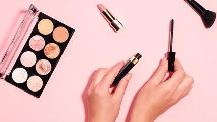 Woman hands holding open black mascara on pastel pink background, top view. Minimal beauty background with makeup products, flat lay, copy space. Eye and face make up concept