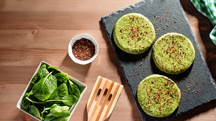 Raw green chicken and spinach burgers with spices on a stone plate in hard light, top view. Eating healthy concept, top view