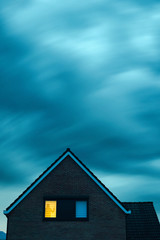 Burglar with handgun in ominous house with illuminated window under stormy sky at dusk.