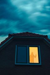 Obraz premium Burglar with handgun in ominous house with illuminated window under stormy sky at dusk.