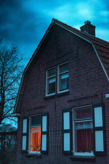 Ominous house with illuminated window under stormy sky at twilight.