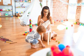 Beautiful teacher and toddler playing around lots of toys at kindergarten