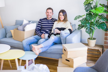 Fototapeta na wymiar Young beautiful couple sitting on the sofa drinking cup of coffee at new home around cardboard boxes