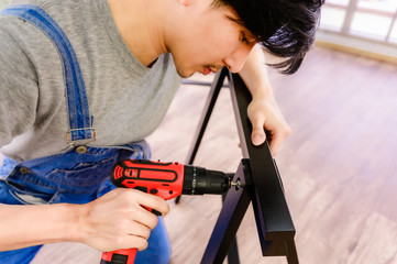 Asian handyman assembling steel table using cordless screwdriver driving screw fix