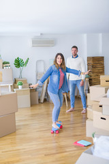 Fototapeta na wymiar Young beautiful couple playing with skate at new home around cardboard boxes