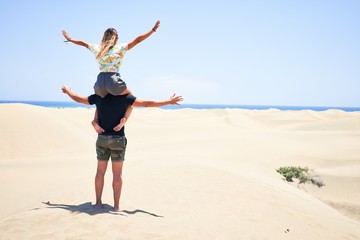 Young beautiful couple smiling happy and confident. Woman sitting on man shoulders with smile on face at the beach