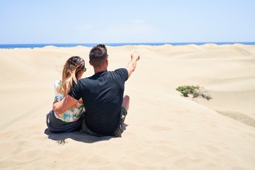 Fototapeta premium Young beautiful couple at sitting backwards and hugging at the beach