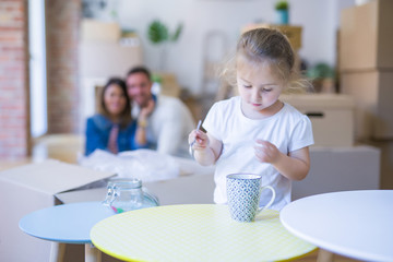 Beautiful family sitting on the floor playing with his kid at new home around cardboard boxes