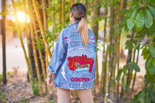 Young beautiful woman wearing denim jacket standing backwards at the town park