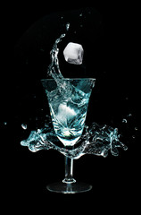 Glass cup with water splashes and ice cubes in the dark room