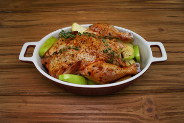 Baked whole chicken with apples and spices in the baking dish on wooden table. Close up