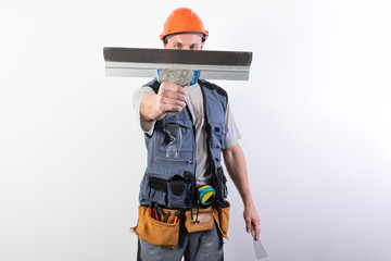 The builder hides his face behind a spatula. In work clothes and hard hat. On a light gray background.