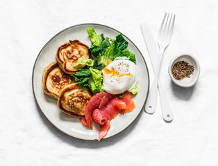 Delicious healthy brunch - poached egg, smoked salmon, green salad and savory pancakes on a light background, top view