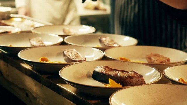 The chef puts food on plates. Pours yellow sauce on fish or meat. Club, restaurant. Yellow sauce is poured on a salmon in a faience plate.