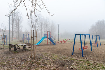 Fototapeta premium Novi Sad, Serbia - January 16, 2020: Children's playground with fog. Empty playground with carousels and swings in misty park.