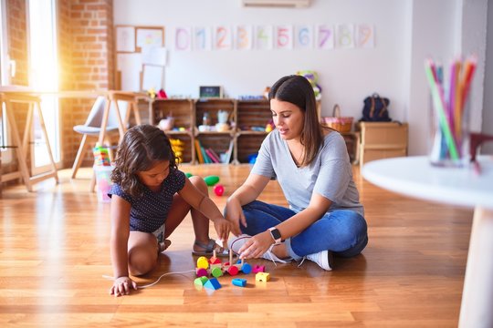 Beautiful teacher and toddler girl playing with train at kindergarten