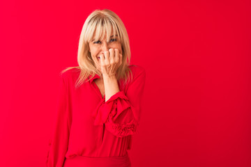 Middle age woman wearing elegant shirt standing over isolated red background looking stressed and nervous with hands on mouth biting nails. Anxiety problem.