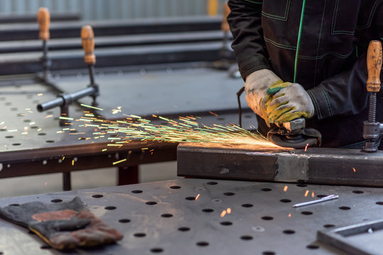 Worker grinding the junction between two sections of a metal square tube with circular grinder in a workshop
