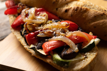 Vegan sub sandwich with grilled vegetables on wooden background