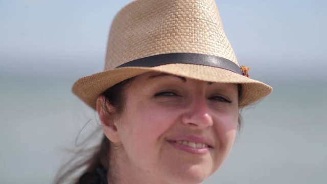 Portrait of a happy woman in a hat on the beach looks at the camera and smiles