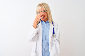 Middle age doctor woman wearing glasses and stethoscope over isolated white background smelling something stinky and disgusting, intolerable smell, holding breath with fingers on nose. Bad smells 