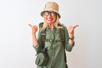 Middle age hiker woman wearing backpack hat canteen glasses over isolated white background success sign doing positive gesture with hand, thumbs up smiling and happy. Cheerful expression and winner