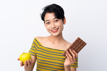 Young Asian girl taking a chocolate tablet in one hand and an apple in the other