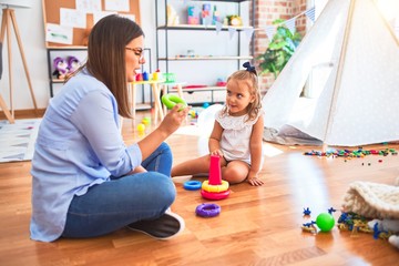 Caucasian girl kid playing and learning at playschool with female teacher. Mother and daughter at playroom playing with inteligence toys