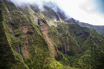 Aerial view of Kauai's lush colorful interior mountain landscape. Weeping waterfalls dot the landscape. 