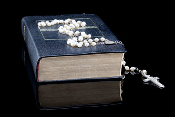 Bibel mit Goldschnitt, Rosenkranz isoliert auf schwarzem Hintergrund mit Spiegelung und Platz für...