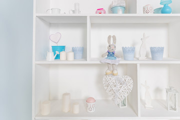 Wooden box with cells filled with Easter decor. bookcase with easter toys, candles, vases.shelves with soft toys rabbits in the design of the children's room.rabbit dolls.Display cabinet with