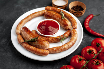grilled sausages with spices and tomatoes on a white plate on a stone background, close-up