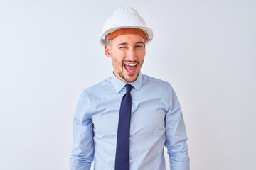 Young business man wearing contractor safety helmet over isolated background winking looking at the camera with sexy expression, cheerful and happy face.