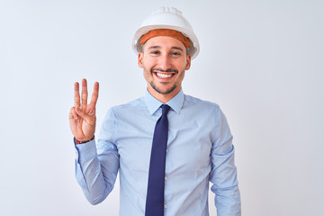 Young business man wearing contractor safety helmet over isolated background showing and pointing up with fingers number three while smiling confident and happy.
